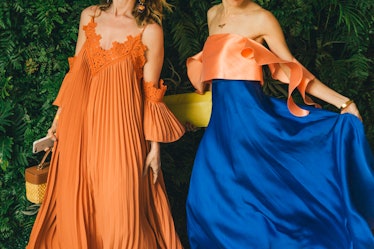 A woman in an orange pleated dress next to a woman in an orange-and-blue satin dress at Veuve Clicqu...