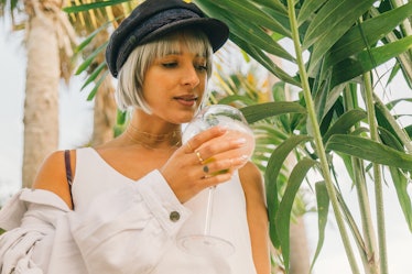 A woman wearing a white shirt and a black cap having a drink at Veuve Clicquot’s Third Annual Carnav...