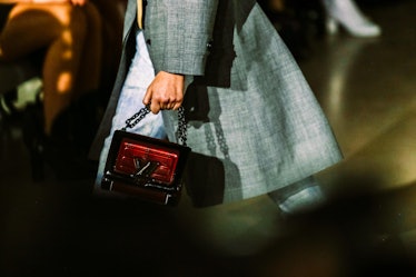A model in a grey coat holding a burgundy handbag from Louis Vuitton’s Fall 2017 collection walking ...