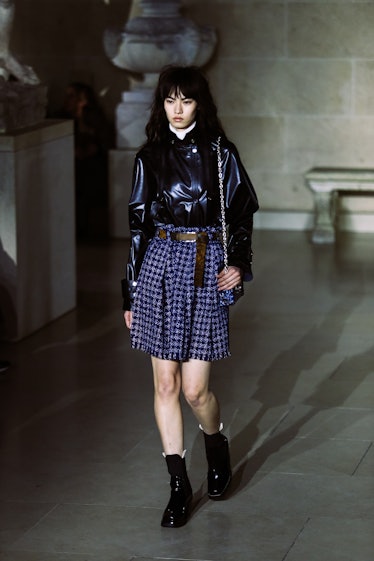 A model in a blue plaid skirt and a black leather shirt walking the runway during Louis Vuitton’s Fa...