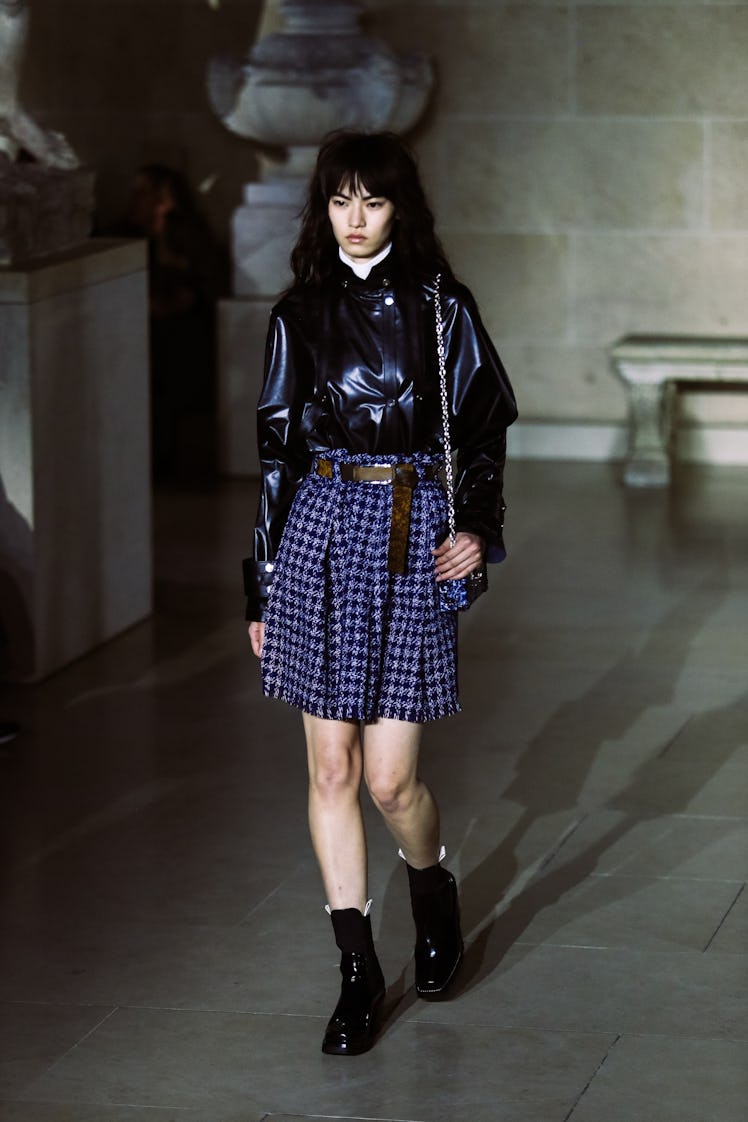 A model in a blue plaid skirt and a black leather shirt walking the runway during Louis Vuitton’s Fa...