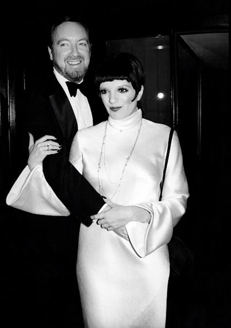 Liza wears a dramatic white silk dress with bell sleeves and high collar.