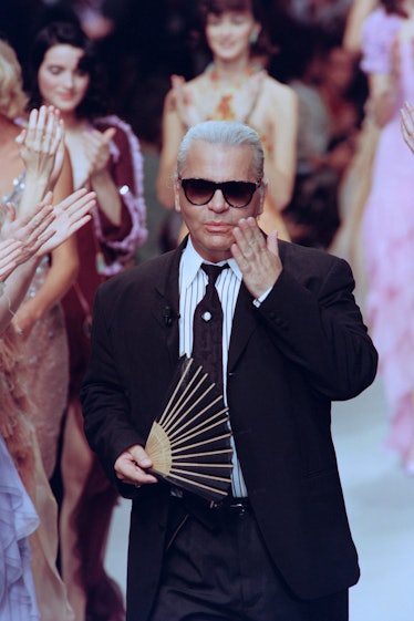 Karl Lagerfeld walking down the runway blowing a kiss with a hand fan in his other hand while the mo...