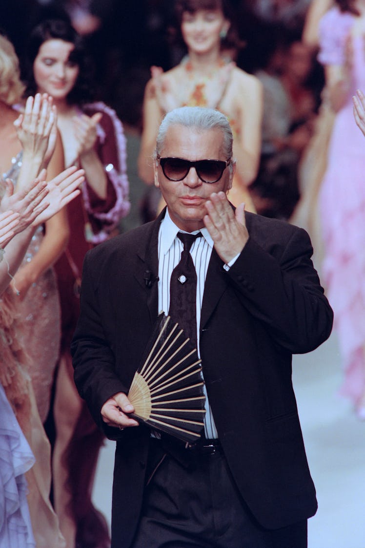 Karl Lagerfeld walking down the runway blowing a kiss with a hand fan in his other hand while the mo...