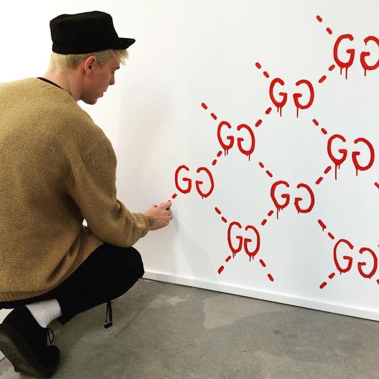Trevor Andrew spray painting Gucci logos in red on a white wall 