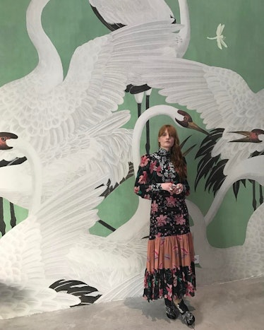 Florence Welch posing in a black flower-patterned Gucci dress, against a green wall with swans on  i...