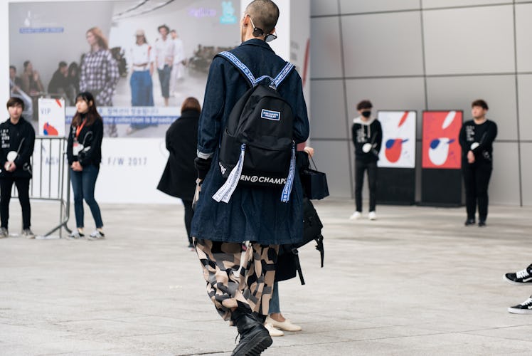 A person wearing a blue trench coat, camouflage pants, black lace-up boots, and a backpack during Se...