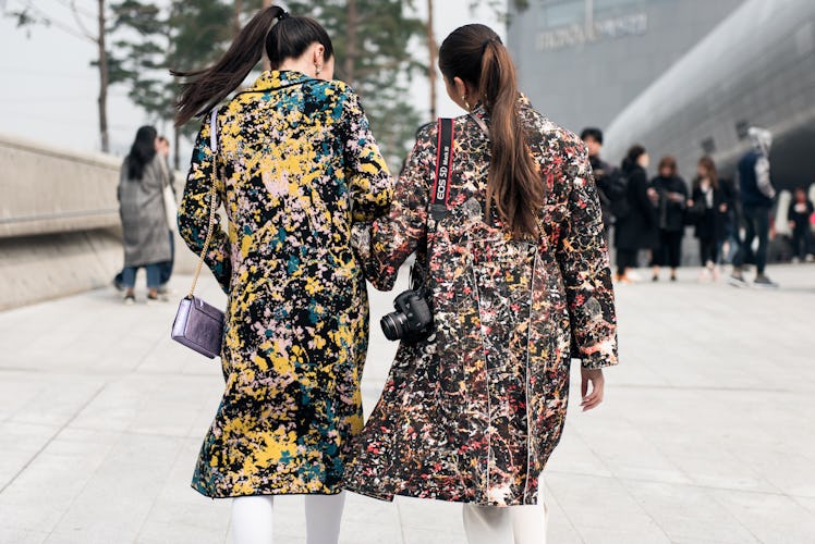 Two women wearing matching coats in different colors during Seoul Fashion Week.