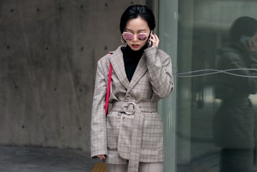 A woman wearing a black turtleneck and a checked blazer in beige hues paired with beige pants, talki...