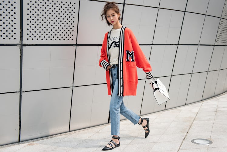 A woman wearing jeans, a white t-shirt and an orange cardigan walking the street of Seoul.