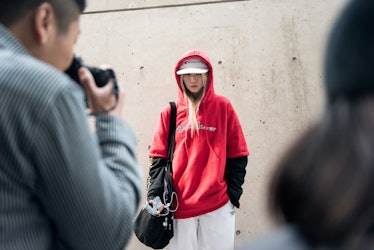 A woman wearing a white cap, track pants, and a red hoodie while posing for a photo.