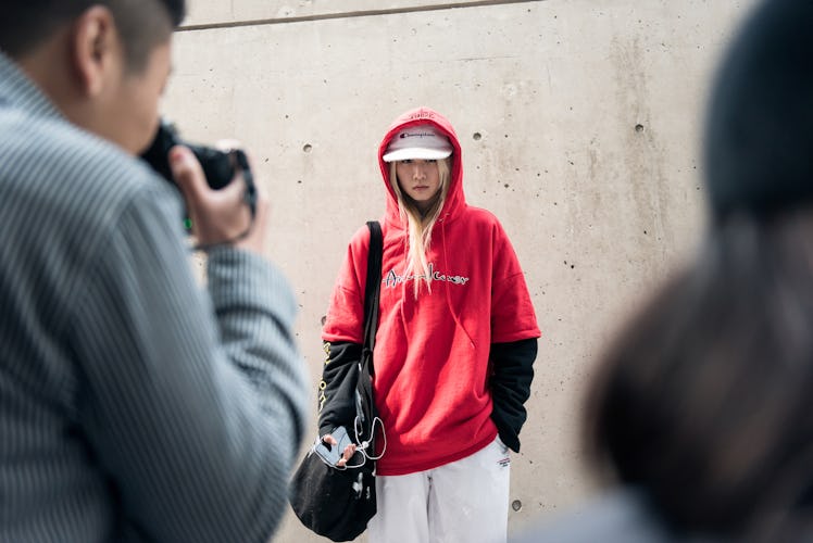 A woman wearing a white cap, track pants, and a red hoodie while posing for a photo.