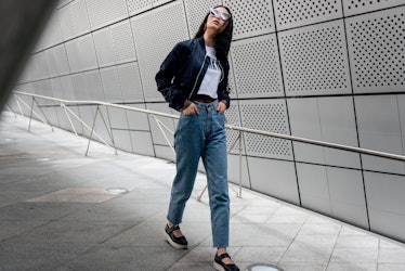 A woman wearing denim jeans, a white t-shirt and a black bomber jacket while walking in Seoul.
