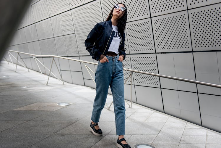 A woman wearing denim jeans, a white t-shirt and a black bomber jacket while walking in Seoul.