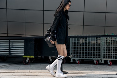 A woman wearing a black hoodie, white knee-high socks and sneakers while walking in Seoul.