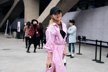 A girl wearing a black cap and a pink stripy shirtdress smiling for a photo during Seoul Fashion Wee...