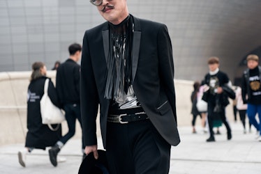 A man in a black suit posing for a photo during Seoul Fashion Week.