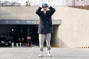 A person wearing grey track pants, black coat and a blue cap on the streets of Seoul.