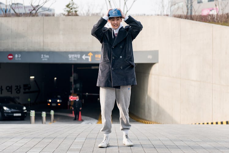 A person wearing grey track pants, black coat and a blue cap on the streets of Seoul.