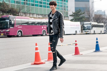 A man wearing a black leather jacket, black ripped jeans, and a stripy t-shirt while walking the str...