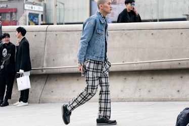 A man in a denim jacket, checked shirt and a matching pants walking the street of Seoul.