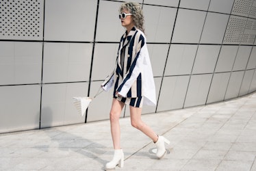 A woman walking in a black-and-white stripy two-piece set, white ankle boots and a matching bag.