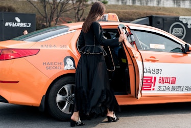 A woman wearing an all-black outfit getting into a taxi during Seoul Fashion Week.