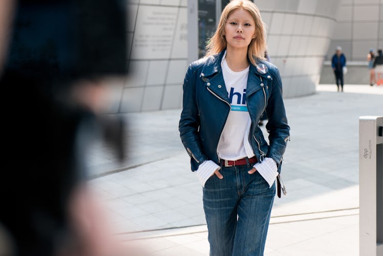 A woman wearing a white t-shirt, blue jeans and a blue leather jacket walking the street of Seoul.