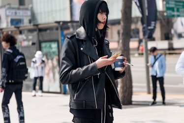 A girl in an all-black outfit drinking coffee and smoking on the street of Seoul.