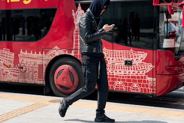 A man wearing an all-black outfit walking next to a bus in Seoul.