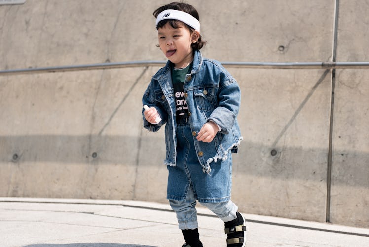 A toddler wearing a denim jacket and skirt and a white headband.