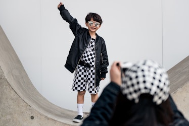 A toddler boy in a black-and-white checked two-piece set and a black leather jacket, posing for a ph...