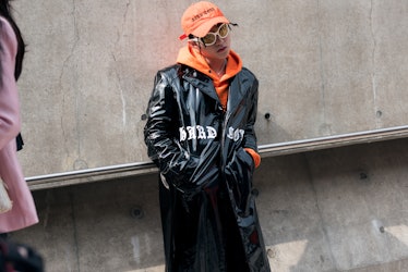 A woman wearing an orange cap, a matching hoodie with a faux black leather coat over during Seoul Fa...