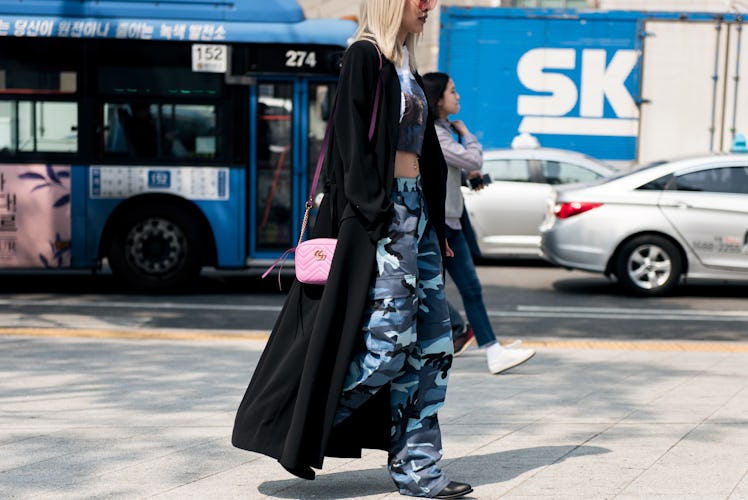 A woman walking the street in Seoul in blue camouflage pants, a matching crop top and a black maxi c...