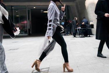 A woman wearing black tights, a grey plaid cut-out blazer with beige sandals walking the street in S...