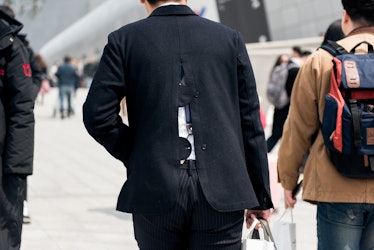A man wearing a black blazer with an open back walking the street of Seoul.