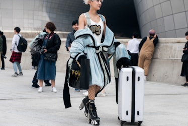A woman in a light blue plush coat, a white top, fishnets and black chunky boots pushing a white sui...