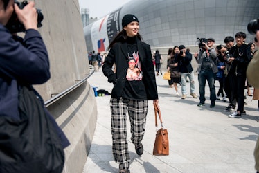 A woman wearing a black beanie, a graphic tee with plaid pants posing for a photographer in Seoul.