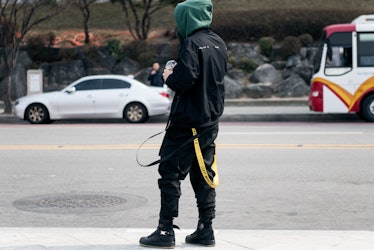 Stylish man in black cargo pants, jacket, and sneakers, sporting a green hoodie, on a Seoul street.