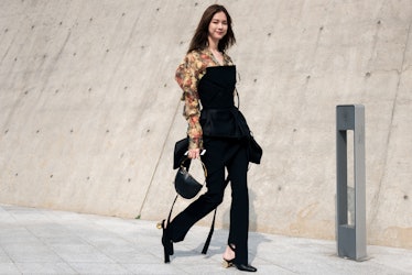 A woman wearing a black jumpsuit with a floral shirt walking the street in Seoul.