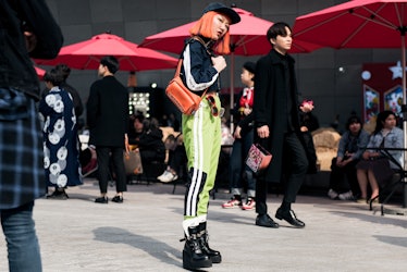 A woman with orange hair opting for a lime green track pants, black jacket and chunky black boots du...