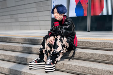 A woman in platform sneakers, black pants with pink birds print and a leather jacket sitting on the ...