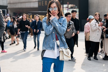 A woman wearing a denim jacket, a white t-shirt and blue track pants posing on the street of Seoul.