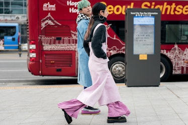 A woman wearing a pink jumpsuit with a black turtleneck walking the street of Seoul.