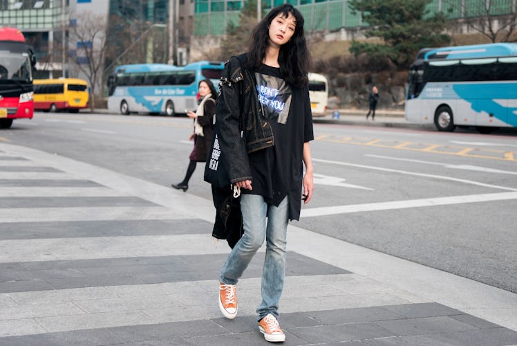 A woman wearing a black graphic tee, denim jeans and orange Chuck Taylor shoes walking the street of...