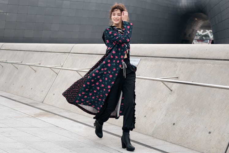 A woman in black pants and a floral coat walking the street of Seoul.