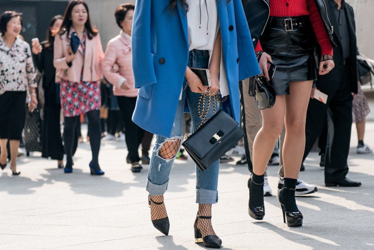 A woman wearing ripped jeans, fishnets, black heels and a blue coat during Seoul Fashion Week