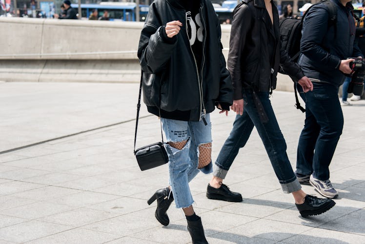 A woman in black ankle boots, ripped jeans with fishnets and a black bomber jacket