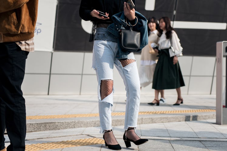 A woman walking in ripped jeans and fishnets during Seoul Fashion Week