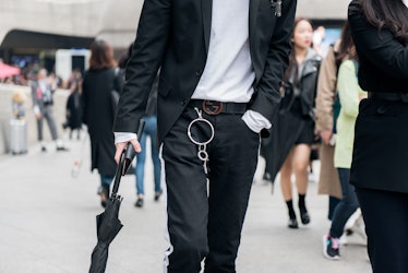 A man in a black suit with chain detail on his belt walking on the street in Seoul.